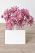 Blank paper card and beautiful pink flowers bouquet in vase on table in natural beige colors