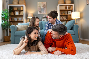 Wall Mural - Happy parents and their small kids talking while lying on carpet at home.