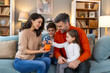 © Graphicroyalty - Happy family cheerful mother and father with kids smiling and putting coins into piggy bank while sitting on sofa at home