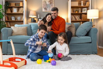 Wall Mural - Cute kids playing while parents relaxing sofa at home together, smiling active boy entertaining with toy car near his sister on floor, happy family spending time together in living room on weekend