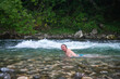 Man with long hair enjoying a refreshing swim in a stunning mountain river amidst rocky landscape