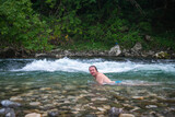Fototapeta Tęcza - Man with long hair enjoying a refreshing swim in a stunning mountain river amidst rocky landscape