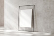 Large blank frame leaning against a textured wall, with natural light casting soft shadows