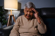 senior woman having a headache pain while sitting on sofa in living room at night