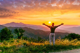 Fototapeta Na sufit - rejoicing man with beautiful scenic mountain sunset landscape on background. happy man watching amazing evening sunset