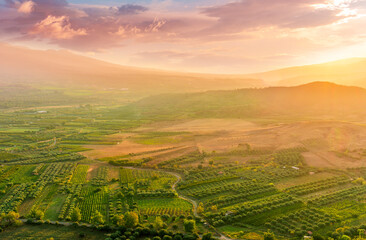 scenic rustic landscape with green hills and farms in a mountain valley during colorful cloudy sunset