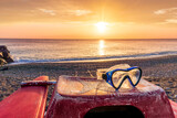 Fototapeta Na sufit - beautiful cloudy morning landscape with diving mask on a red old boat on foreground, sand beach, blue sea with surf and waves and cloudy sunset or sunrise on background