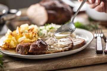 Wall Mural - A close-up view of a spoon with sauce that pours over the meat, roasted neck. As a side dish to the meat are baked potatoes and jasmine rice.