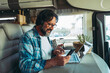 © simona - Traveler modern online people job business lifestyle. One happy mature man using phone and computer inside a camper van motorhome vehicle. Vacation travel and roaming connection technology worker