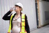 Fototapeta Tęcza - Portrait Happy caucasian logistic engineer pregnant woman working and drinking water at container site	