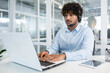 © Liubomir - A young, professional man wearing a headset focuses intently on his laptop in a modern office environment, suggesting productivity and business communication.