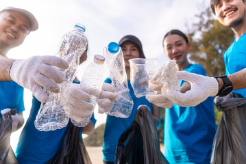 Plastic pollution and environmental problem concept. Happy asian diverse group of volunteers with garbage bags wearing blue t-shirt and cleaning plastic on the beach. Volunteers collecting trash.