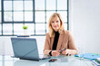 Blond haired businesswoman sitting at desk and using laptop at the office