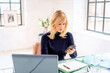 Blond haired businesswoman sitting at desk and using cellphone at the office