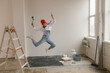 © Westend61 - Cheerful woman with paint equipment jumping in front of white wall at new home