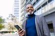 © Westend61 - Happy businessman standing with smart phone in front of building