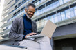 © Westend61 - Smiling businessman working on laptop near building