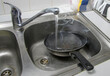 A hot, steaming frying pan immersed in water in a kitchen sink. A frying pan that has not cooled down under cold water