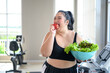 Overweight Asian female happy to eat organic apple for healthy in gym. Weight loss workout, healthy lifestyle concept.