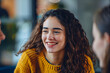 © Welle Photos - A young woman is smiling while sitting and talking to a female friend in a meeting room.