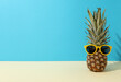 Pineapple with yellow sunglasses on blue background, space for text