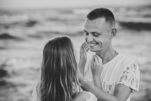 Happy Couple Looking At Each Other Walking On Seashore. Girl Hands Hugs Boy's Face And Looks Into Eyes And Enjoy. Man And Woman Stand On Sand Sea. Female And Male On Beach Ocean. Black And White Photo