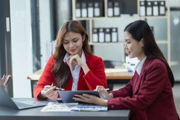 Two asian businesswoman working and brainstorming in workshop and analyzing marketing reports startup project infographics in the office, Sales and business plans, presentation ideas concept.
