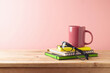 Home office concept with colorful coffee cup,  notebook and eyeglasses on wooden table over pink background