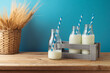 Jewish holiday Shavuot concept with milk bottles, wooden box and wheat ears in basket on wooden table over blue background