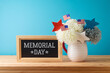 Memorial day concept with flowers decoration, chalkboard and USA flags on wooden table over blue background