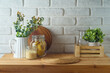 Empty wooden kitchen table with wicker place mat, food jars and plants over white brick wall  background.  Kitchen mock up for design and product display.