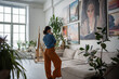 Painter woman looking at painting in artist creative cozy studio. Artist apartment gallery Interior with pot flowers, big sofa, easel, many paintings on wall. Painter home exhibition. Artwork hobby