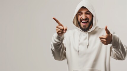 Joyful bearded man in a white hoodie pointing and giving thumbs up against a light background.