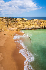 Wall Mural - Vertical view of cliffs and ocean waves crashing onto beach near Albufeira, Portugal