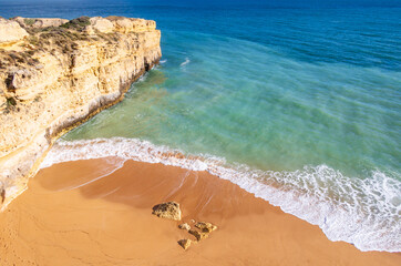 Wall Mural - Top view over ocean and wave crushing on sandy beach in Algarve, Portugal