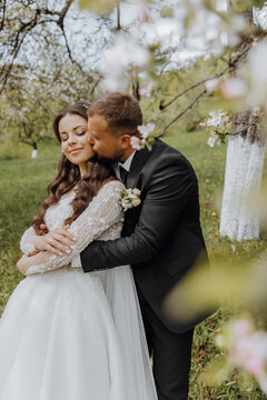 the first meeting of the bride and groom in a blooming garden. The bride in an incredible white dress with expensive hair and makeup. The groom in a black suit goes to the bride
