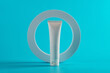Plastic white tube for cream or lotion. Skin care or sunscreen cosmetic with stylish props on blue background.