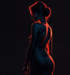 woman in a backless dress is shown from the hips up, lit by red light against a black