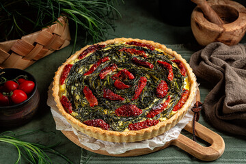 Wall Mural - Italian rustic savory pie made with pie crust, salsola soda or agretti, ricotta cheese, eggs and dried tomatoes on a green wooden table. Homemade baked food.