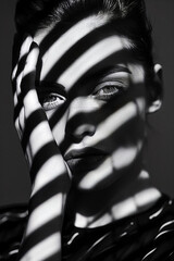 Black and white photograph of an elegant woman with her face partially covered in shadows in the shape of stripes, creating intricate patterns on her skin. 
