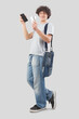 young man smiling and handsome showing mobile phone and credit card dressed in jeans and t-shirt with shoulder bag, isolated on gray background