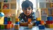 © iuricazac - Young child engrossed in play with colorful wooden blocks sitting on floor in brightly lit room filled with toys and furniture focused gaze on camera.