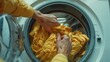 Person's hands reaching into a front-loading washing machine to remove yellow laundry.