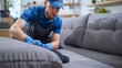 Man in blue uniform cleaning gray couch with blue gloves.