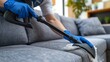 Person wearing blue gloves using a vacuum cleaner to clean a couch.