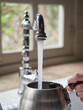 close-up view, water flowing out of the kitchen faucet to fill stainless steel pot held by the handle with one hand.
