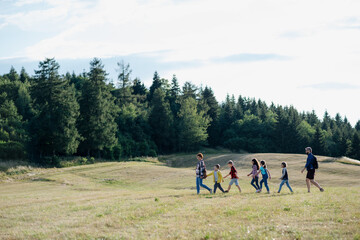 Poster - Young students walking across meadow during biology field teaching class, holding hands. Dedicated teachers during outdoor active education teaching about ecosystem, ecology.