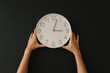 © VISTA by Westend61 - Hands of woman holding wall clock against black background