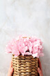 Wicker basket with pink flowers in womans hands over stone table. Flat lay, top view.