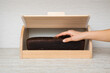 Young adult woman hand holding fresh dark brown rye bread and taking out from wooden bread box on table top at home kitchen. Closeup. Front view.